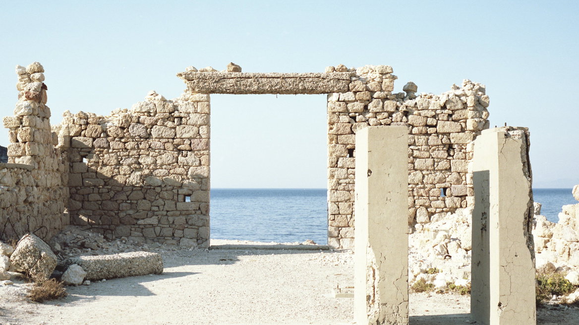 The island of Milos – the ruins of an old building, the figure of an old man in the middle, the sea and the sky on the horizon, and rocks eroded by the wind