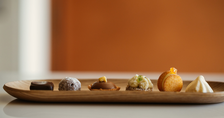 Presentation of one of La Gaia's passes, with small sweet morsels on a light wooden plate