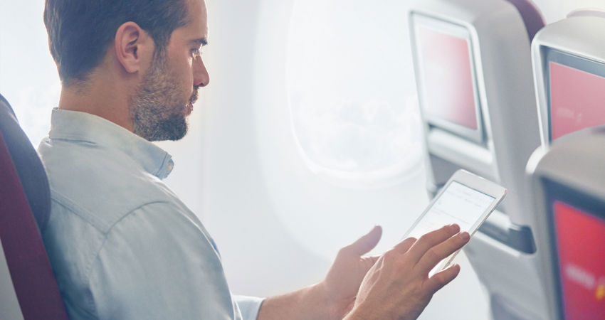 Avios Wallet: suma los Avios de Iberia y de Vueling. En la imagen, un pasajero comprueba su cuenta de Iberia Plus en una tablet, sentado en cabina.