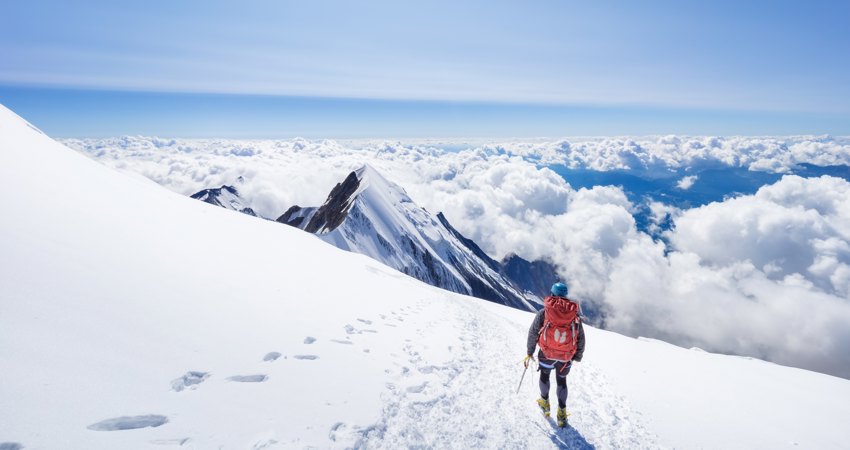 Travel to Geneva for 9000 Avios. In the picture, a mountaineer looks out over the Alps from one of the highest peaks, surrounded by clouds.