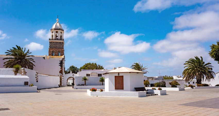 En la imagen, una de las plazas de Teguise, con edificios y casitas encaladas justo a verdes palmeras