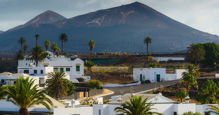 En la image, el pueblo de Yaiza en primer plano, con casitas bajas encaladas, enmarcado por el perfil de uno de los volcanes de la isla.