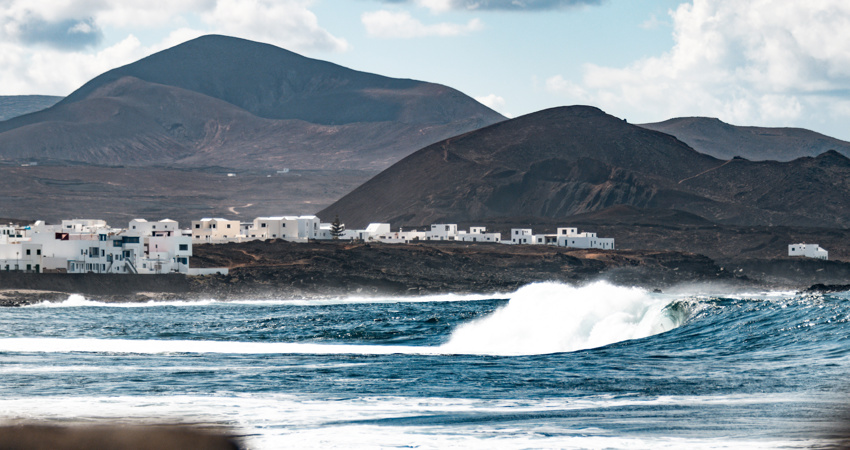 En la imagen, el perfil de La Santa de fondo, sobre un paisaje lunar. En primer plano, las olas de un bar embravecido, perfecto para el surf 