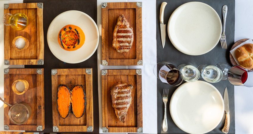 Overhead view of a table at Don Julio, with wines, meats and roasted sweet potato, as well as soup and bread accompaniments