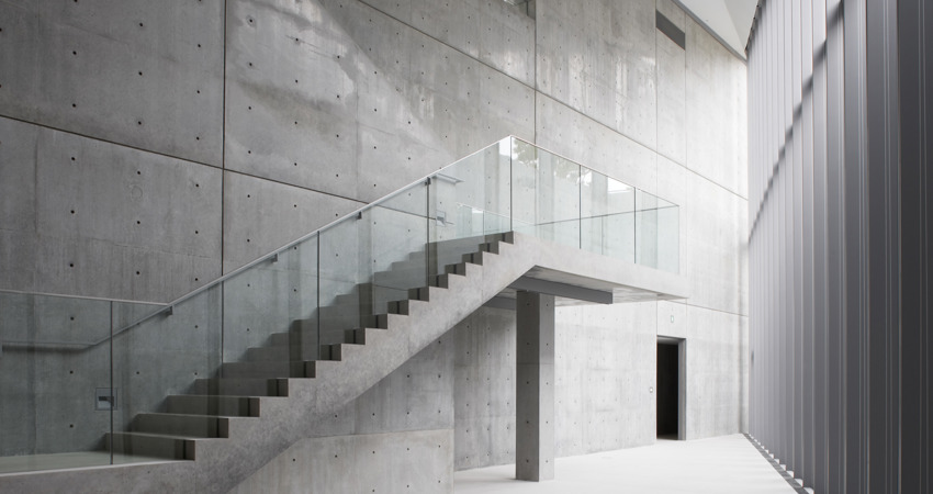 In the image, the inner vertex where the two outer walls of the building, made of concrete, steel and glass, meet. A flight of stairs leading nowhere and a door opening into a mysterious room can also be seen