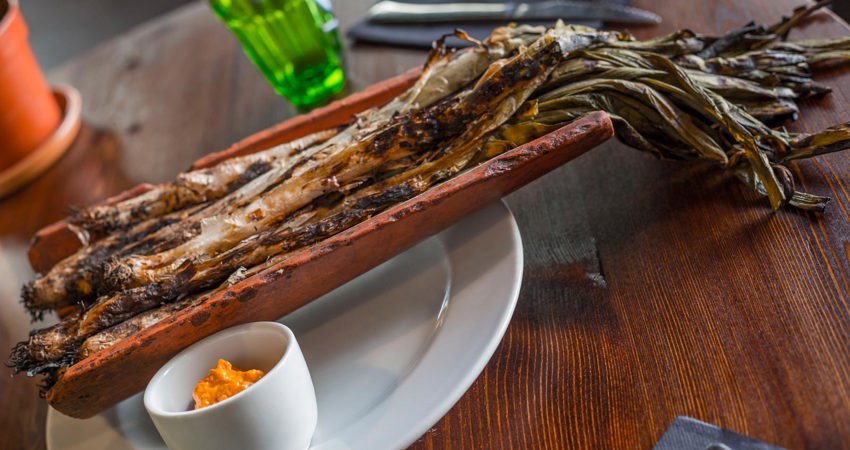 Imagen de la calçotada típica de Casa Masana, con los calçots servidos sobre una teja en medio de la mesa
