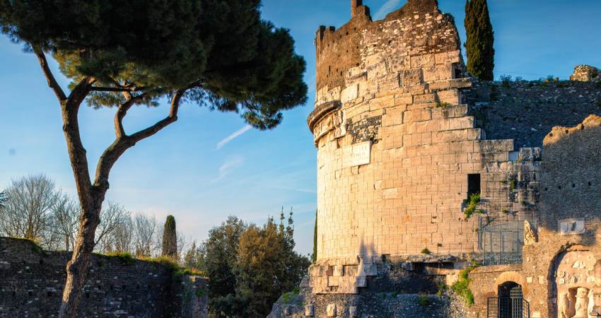 El Mausoleo de Cecilia Metela al atardecer, con la estructura circular y restos de la muralla medieval, rodeado por árboles