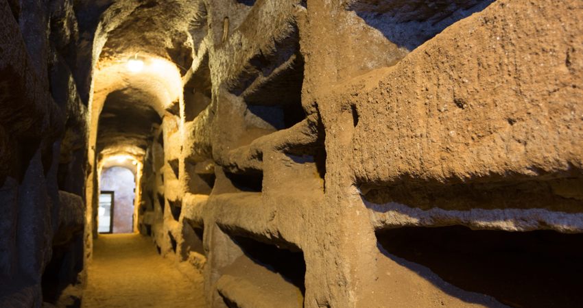 Largo pasillo arqueado en las catacumbas, con hornacinas, probablemente dedicadas a la sepultura de fieles, a cada lado.