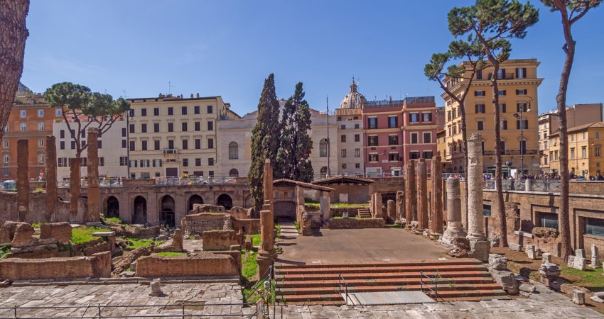 In the picture, Largo di Torre Argentina, with the steps where Caesar was assassinated on the right side of the panorama and columns, arcades and vegetation on the left side. Rome's buildings frame the landscape
