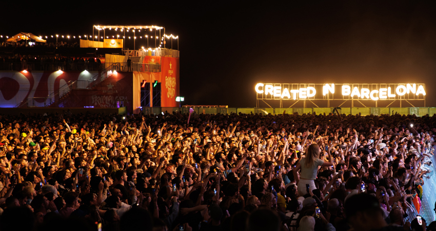 Primavera Sound 2025. En la imagen, es noche cerrada y puede verse a miles de persona bailando y cantando frente a un escenario. Al fondo, un cartel con luces de neón amarillas donde puede leerse "Created in Barcelona".