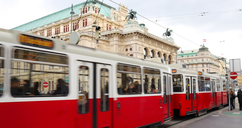 Qué hacer en una escapada a Viena. En la imagen, un tranvía típico de Viena, con su parte superior en blanco y la inferior en rojo, pasa delante de la Ópera Estatal de Viena, reconocible por su fachada renacentista y su tejado de cobre verde