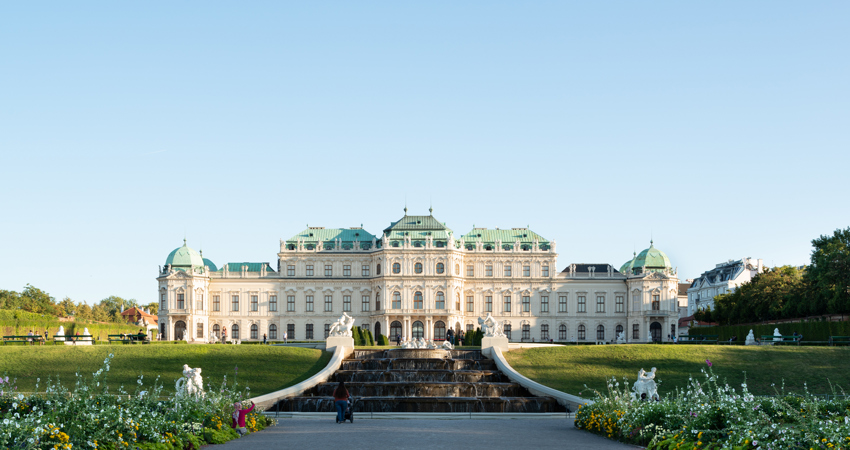 Escapada a Viena. Vista trasera del Palacio Belvedere al atardecer de la primavera. En la imagen puede verse parte del jardín barroco, con un césped perfecto y un camino de gravilla flanqueado por parterres de flores.
