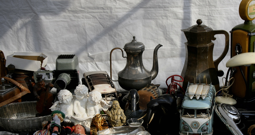 In the image, one of the stalls displays a picture with a classic still life composition. Two silver teapots, a small bust of Tutankhamun, an old camera and a miniature Mercedes van