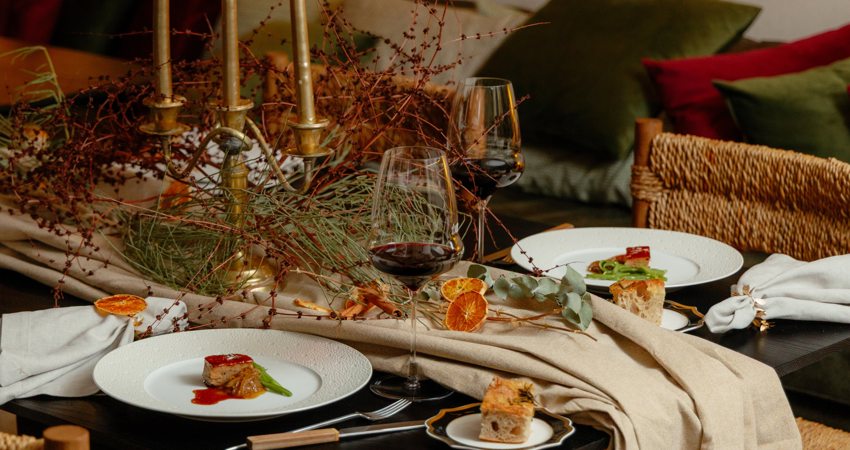 En la imagen, una de las mesas de Gurisa, con uno de los principales platos del menú navideño, vino tinto y pan y un camino de mesa hecho con telas, candelabros plantas otoñales y frutas secas