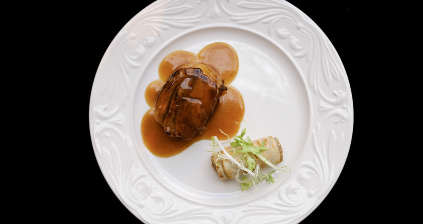 In the image, one of the porcelain plates from the Palace Hotel, on a black background. Sirloin steak in sauce with vegetable side dish.