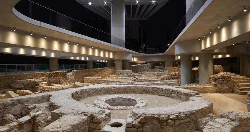 En la imagen. una excavación arqueológica con cimientos de piedra de diferentes estructuras circulares y muros de distintas alturas, todo ello rodeado de pasarelas suspendidas para que los visitantes puedan disfrutar del espacio.